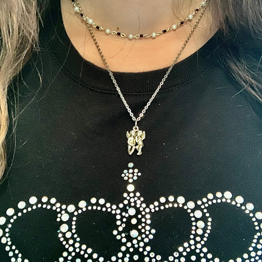 Wearing a beaded black and white necklace and a silver chain necklace with a charm of two angels.