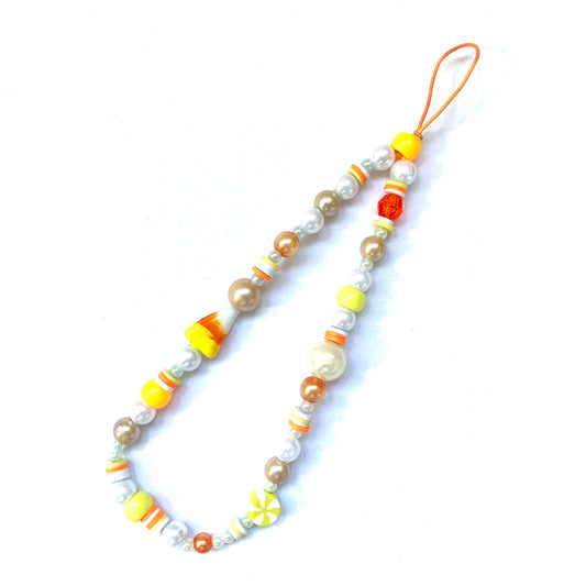 Phone charm with an orange string, orange; white; and yellow beads, and a glass candy corn bead.