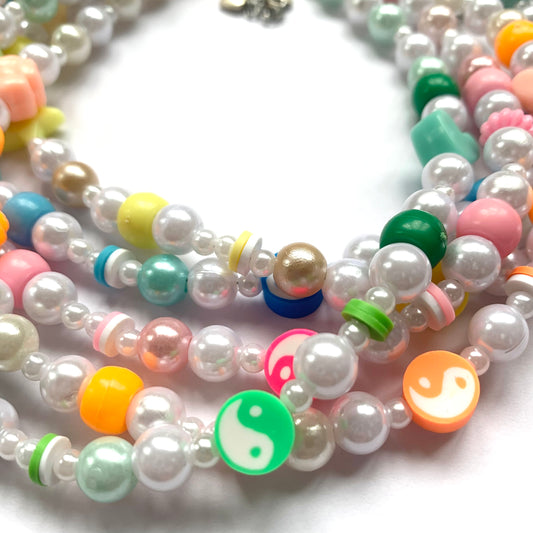 Close-up of pink, orange, yellow, green, and blue beaded yin and yang necklaces.