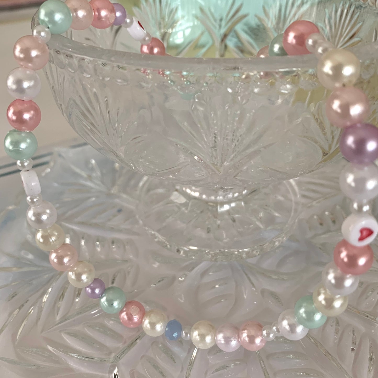 Necklace with white, purple, beige, pink, and mint pearls in a fancy glass goblet.