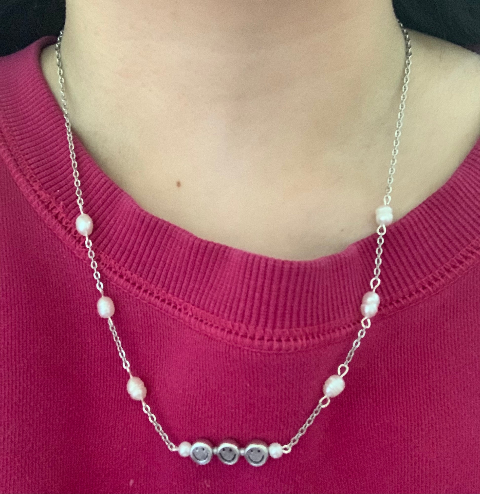 Wearing a silver chain necklace connected by freshwater pearls and a wire with three silver smiley face beads and pearls between each.