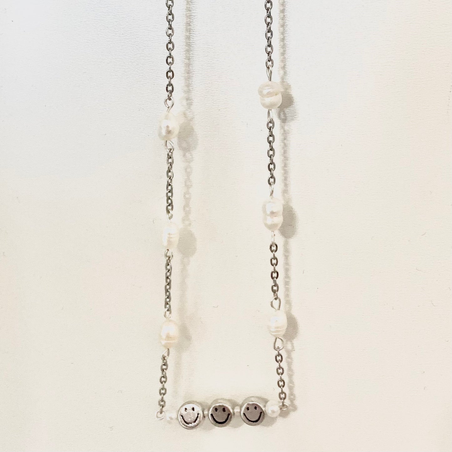 Silver chain necklace connected by freshwater pearls and a wire bar featuring three silver smiley face beads and pearls between each.