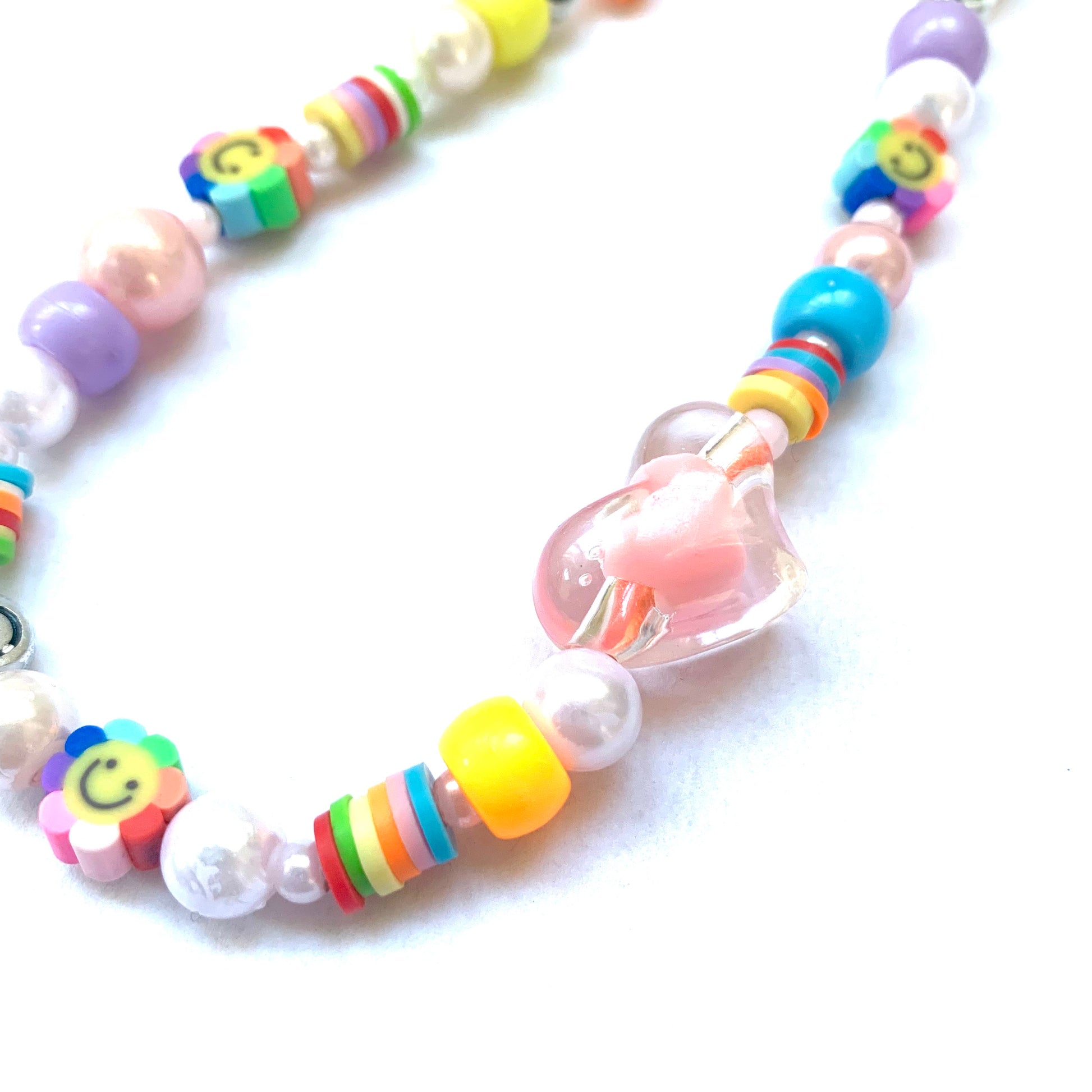 Close-up of large pink heart bead and surrounding beads, including a rainbow smiley flower bead and heishi beads.