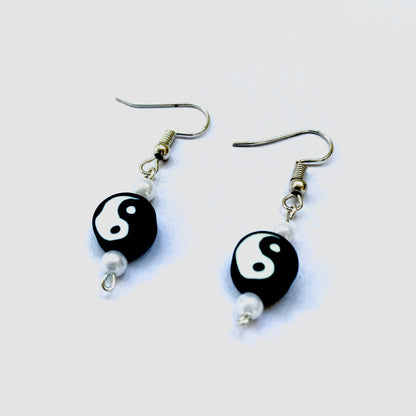 Low-angle shot of a pair of silver fish hook earrings with a black yin and yang polymer bead and two small faux pearls each.