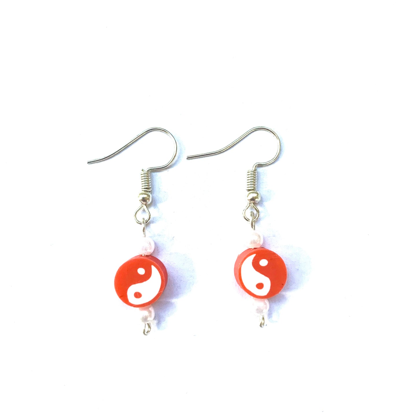 Low-angle shot of a pair of silver fish hook earrings with a red yin and yang polymer bead and two small faux pearls each.