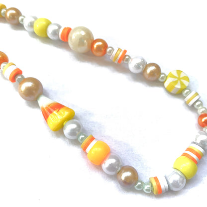 Close-up of a phone charm with a glass candy corn bead and matching orange, white, and yellow beads.