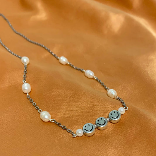 Silver chain necklace connected by freshwater pearls and a wire bar featuring three silver smiley face beads and pearls between each on an orange satin background.