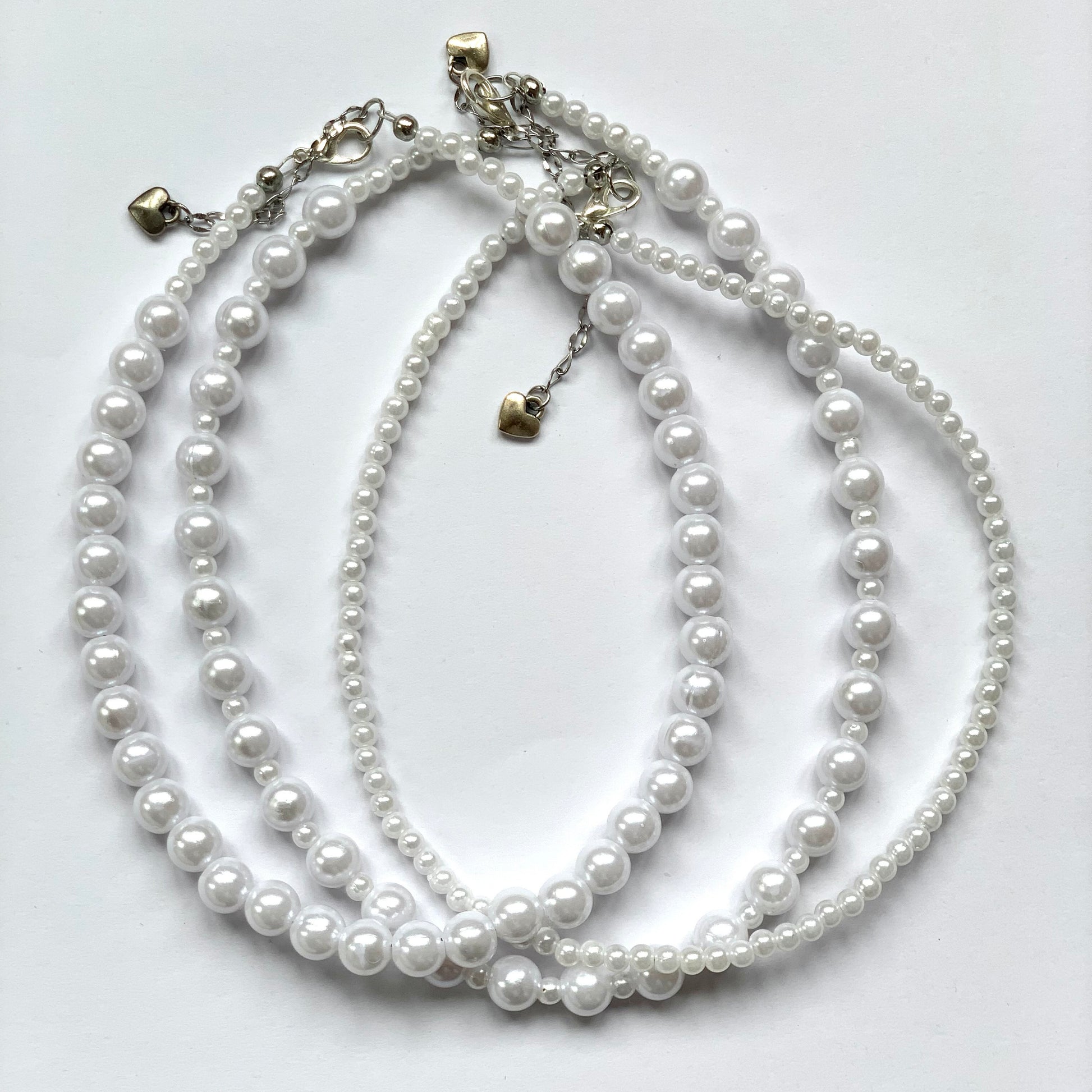 Three beaded faux pearl necklaces: one with large pearls, one alternating between large and small, and one small.